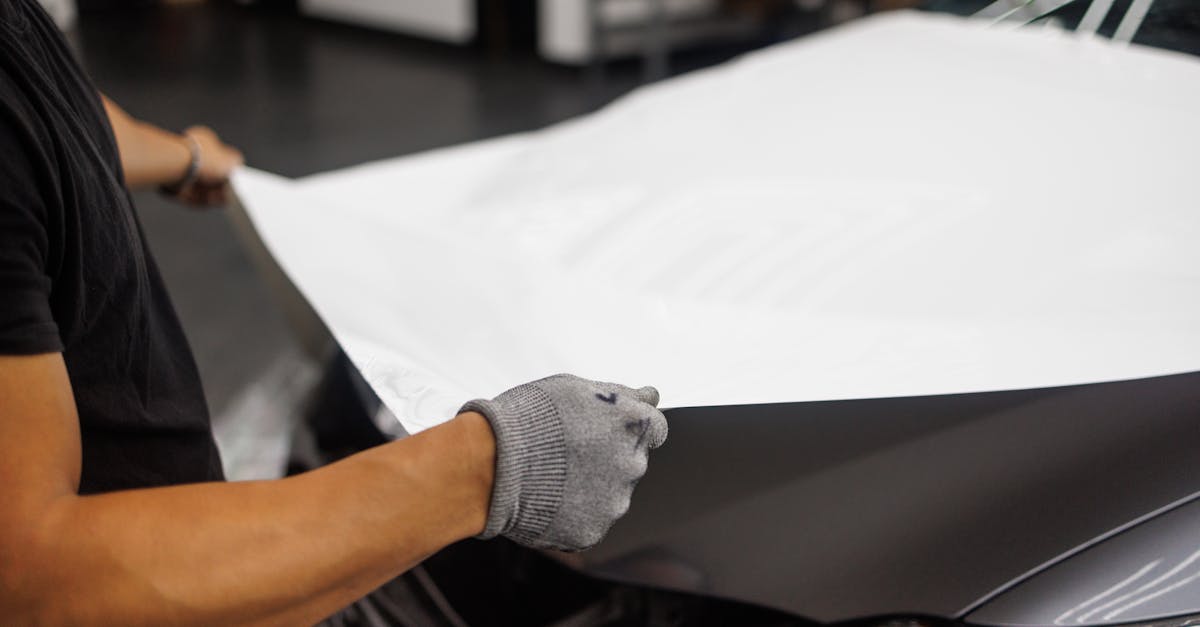 Person applying vinyl wrap to car hood in garage setting.